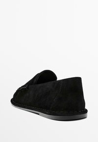 Black suede slip-on shoe with a rounded toe, visible stitching, and a low, textured rubber sole. Simple design, no embellishments.