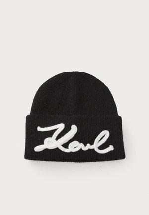 Gorro preto tricotado com dobra na aba, apresentando grande texto bordado em branco, "Karl." Tecido texturizado com ribateado vertical na superfície.