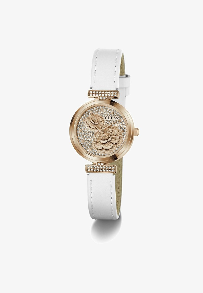 Montre Guess avec boîtier rond doré, bracelet en cuir blanc, cadran à motif floral orné de cristaux et accents argentés. Détails en or rose.