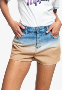 Pantalones cortos de denim con un diseño ombré que transiciona de azul en la parte superior a beige en la parte inferior, con bordes deshilachados y bolsillos frontales.