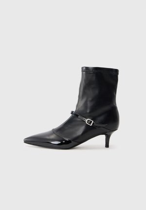 Bottines noires avec un bout pointu et élégant, en cuir brillant. Elles présentent une tige ajustée et une sangle étroite avec une boucle décorative.