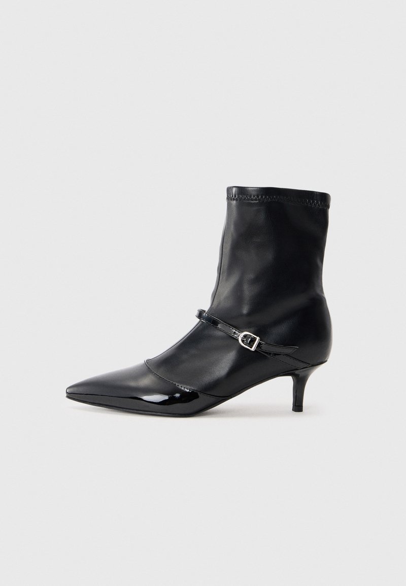 Bottines noires avec un bout pointu et élégant, en cuir brillant. Elles présentent une tige ajustée et une sangle étroite avec une boucle décorative.