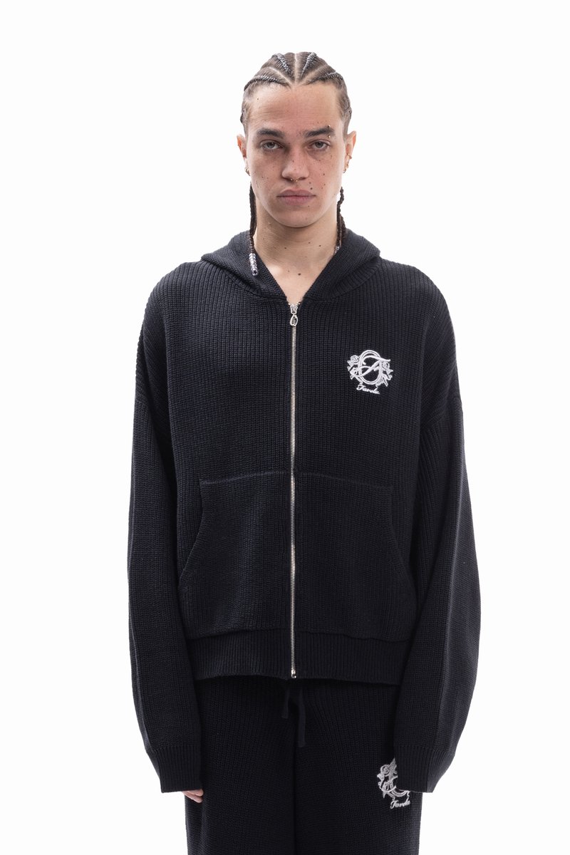 Black zip-up hoodie with a textured knit design, front pockets, and a contrasting white logo on the left chest. Relaxed fit, oversized sleeves.