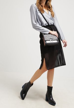 Blusa di raso grigia, gonna midi nera plissettata con spacco, stivaletti neri alla caviglia con tacchi impilati blu e una borsa con dettagli metallici.