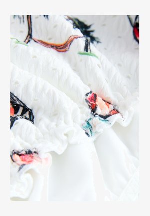 Balta medžiaga su tekstūrinėmis raukšlėmis ir spalvingu gėlių siuvinėjimu, kuriame vyrauja rožinės, raudonos ir žalios spalvų atspalviai ant minkštos fono.