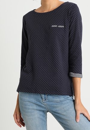 Top a maniche lunghe blu navy con pois, dal collo rotondo, dotato di una piccola tasca sul petto e dettagli a righe sui polsini delle maniche.