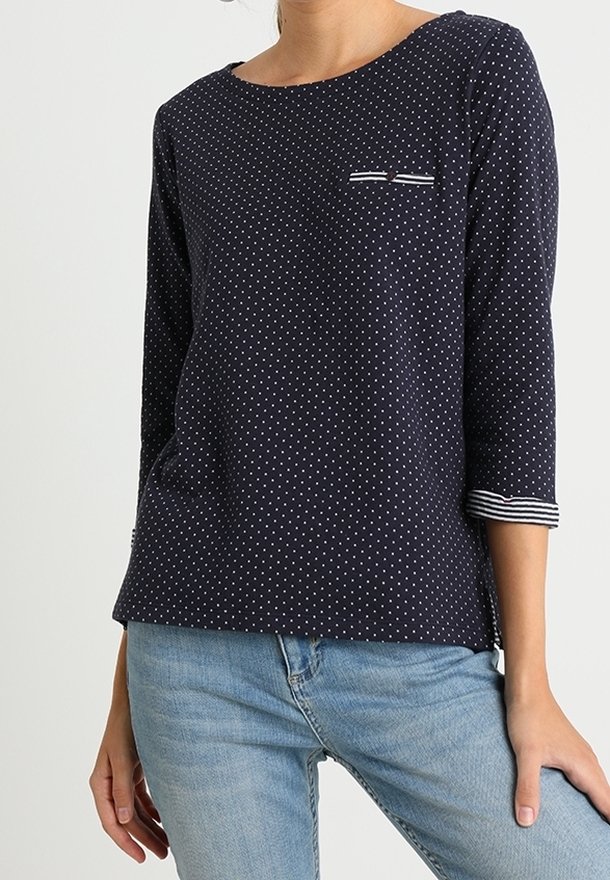 Navy blue polka dot long-sleeve top with a round neckline, featuring a small chest pocket and striped accents on the sleeve cuffs.