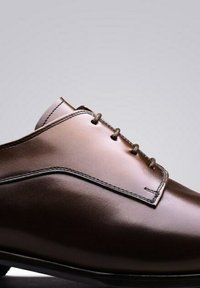 Bruine leren schoen met een gladde textuur, ronde neus en minimalistisch ontwerp, met vier veterogen en contrasterende stiksels.