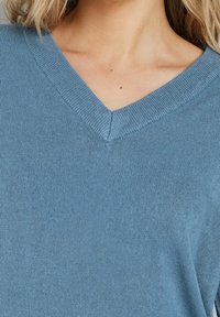 Jasnoniebieski dziergany sweter z dekoltem w serek, charakteryzujący się gładką fakturą i prążkowanym wykończeniem kołnierza. Widok z bliska podkreśla szwy.