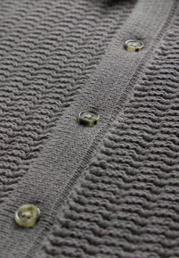 Gray knitted cardigan featuring a textured pattern, five round yellow buttons, and a straight collar design.