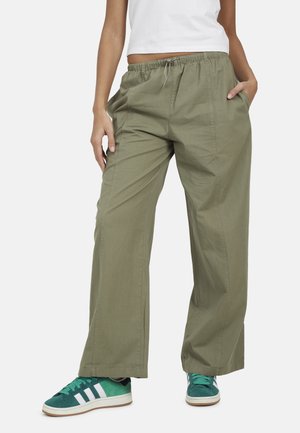 Pantalon vert olive à coupe décontractée avec ceinture élastique et cordon de serrage, associé à des baskets bleu sarcelle et blanches ainsi qu'à un haut blanc court.