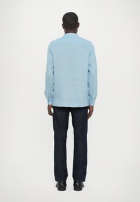 Lys blå skjorte med lange ermer, krage og ensfarget tekstur, kombinert med mørkeblå jeans og svarte sko.