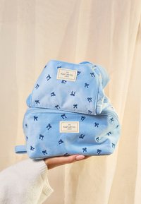 Bolsas de terciopelo azul con bordados de lazo en azul marino. La bolsa más grande tiene un cierre de cremallera, y ambas tienen etiquetas que dicen "The Flat Lay Co."