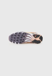 Semelle de chaussure de sport en violet, noir et blanc, présentant des motifs de grip texturés, des formes dynamiques et un détail de marque proéminent en orange.