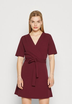 Burgundy wrap dress with short sleeves, v-neck, and tie waist detail. Soft fabric with a smooth texture and flared skirt.