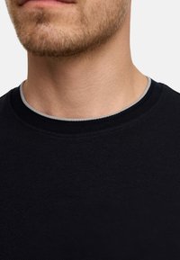 Sudadera negra de cuello redondo con una tela texturizada. El escote presenta un ribete gris en contraste para un detalle adicional.