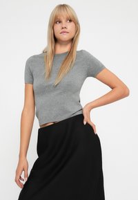 Haut gris à manches courtes en tissu doux avec un design ajusté et un col rond, associé à une jupe noire fluide.