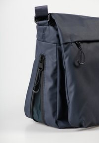 Marineblaue Umhängetasche aus glattem Stoff, mit einer Frontzippertasche und einem umschlagbaren Deckel mit verstellbarem Tragegurt.