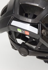 Casco da ciclismo nero con fori di ventilazione, meccanismo di regolazione della taglia e adesivi di certificazione CE. Presenta una finitura opaca e un design ergonomico.