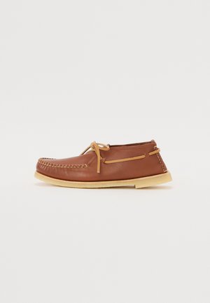 Mocassin en cuir brun avec un bout arrondi, couture décorative, fermeture à lacets et semelle en caoutchouc légère. Texture lisse, design minimaliste.