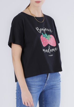 Mujer con camiseta negra con fresas rosas y texto "Bonjour madame", combinada con jeans azules y un collar dorado.