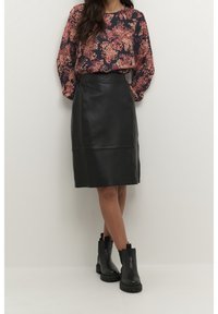 Jupe crayon en cuir noir à texture lisse, associée à un haut à manches longues à motif floral dans des tons foncés. Bottines noires épaisses.