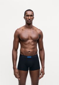 Boxer shorts neri realizzati in tessuto elasticizzato con una cintura blu con etichetta "HUGO". La vestibilità è aderente, con una texture liscia e morbida.