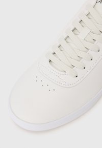 White leather sneaker with round toe, textile laces, and perforated detailing on the vamp. White rubber sole with smooth texture.