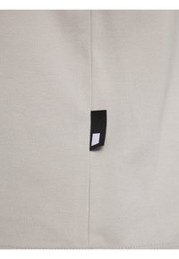 Tessuto beige chiaro con una texture liscia. Presenta un'etichetta nera sul lato con un logo rettangolare bianco. Design semplice e minimale.