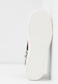 Semelle de chaussure de sport blanche avec un motif géométrique et le logo "Steve Madden" au centre, présentée sur fond blanc.