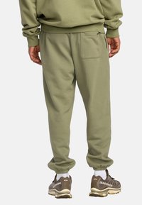 Pantalones de chándal verde oliva con un ajuste relajado, puños elásticos y un bolsillo trasero. La textura de la tela parece suave y cómoda.