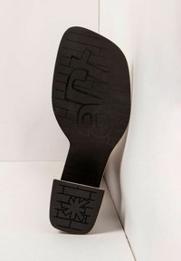 Suela de zapato negra con un patrón texturizado, que presenta un diseño prominente de estrella. El tacón tiene forma cuadrada y está hecho de goma duradera.