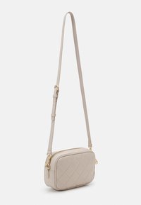 Beige quilted crossbody bag with a rectangular shape, slim leather strap, gold hardware, and a zippered top closure.