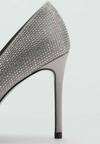 Scarpa con tacco alto grigia, con superficie testurizzata coperta da piccoli chiodi riflettenti. Presenta una punta affusolata e un elegante tacco a stiletto.