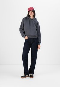 Šedá mikina s kapucňou, tmavomodré džínsy, čierne tenisky s béžovými šnúrkami a ružová čiapka. Neformálny outfit s voľným strihom.