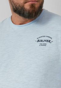 Lichtblauwe t-shirt met korte mouwen van zachte stof, voorzien van een ronde halslijn en een gedrukt logo op de borst. Gladde textuur.