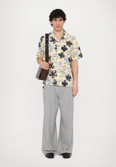 Short-sleeve, yellow shirt with black and blue floral pattern, paired with light gray wide-leg trousers and a brown shoulder bag.