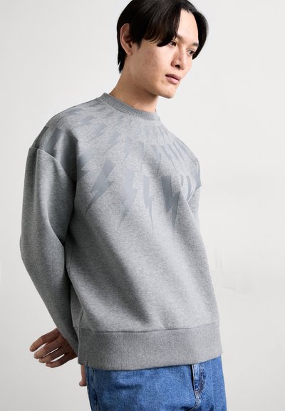 Grå sweatshirt med rund hals, som har ett grafiskt blixtmönster i en ljusare grå nyans på den övre framsidan. Ribbad i ärmsluten och nederkant.