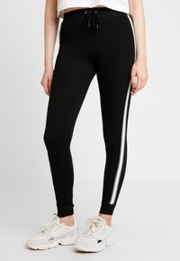 Svarta leggings med en åtsittande design, dragsko i midjan och vita sidosträck. Tillverkade av mjukt material, lämpliga för avslappnad användning.