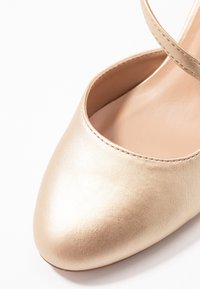 Nude läderballettskor med spetsig tå och ett enkelt ankelband. Slät textur med en subtil lyster. Minimalistisk design.