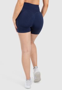 Pantalones cortos de talle alto en color navy con un diseño ajustado, textura suave y detalles de costura acentuados para dar forma. Llevados con zapatillas deportivas blancas.