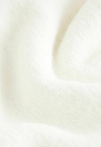 Un tissu doux, blanc, texturé avec une surface moelleuse et légèrement duveteuse. Le matériau semble chaud et accueillant, avec des variations subtiles d'épaisseur.