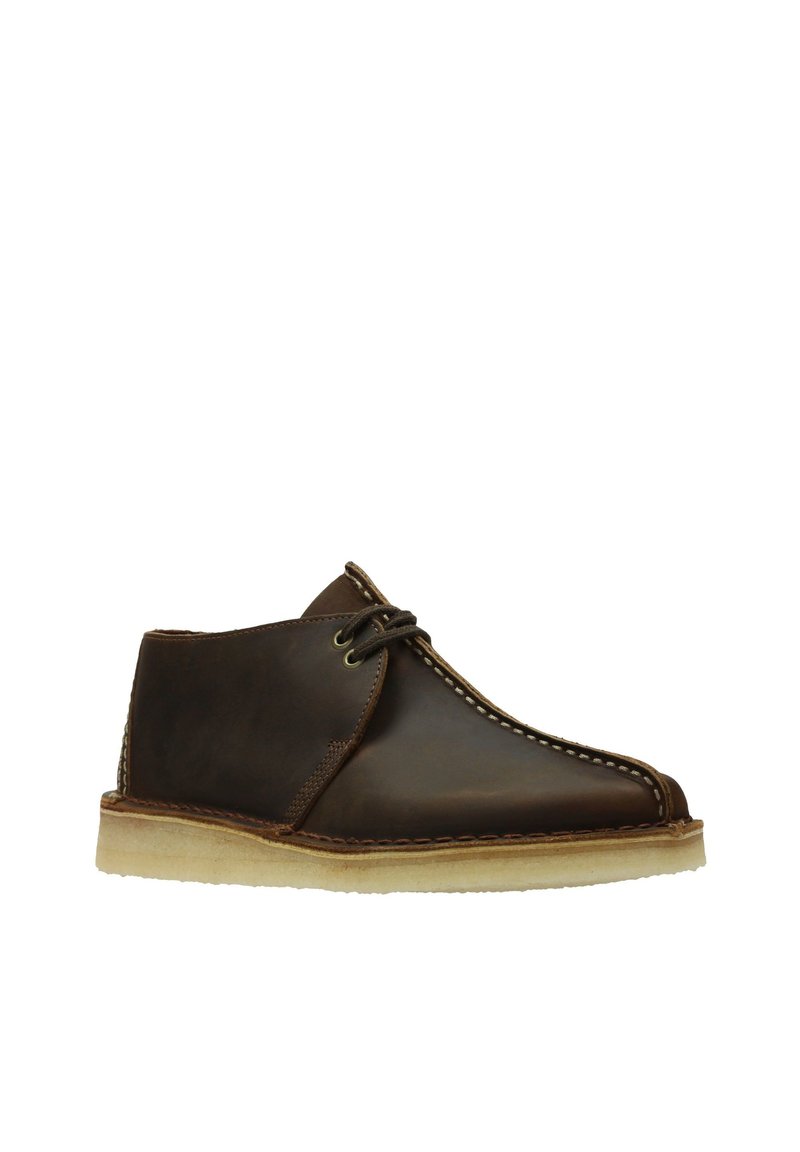 Stivali chukka in pelle marrone con punta rotonda, suola beige e cuciture bianche a contrasto. Presentano un laccio sottile e una texture liscia.