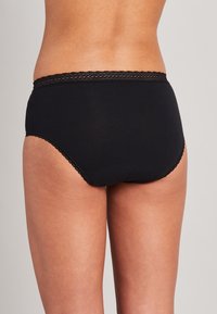 Schwarze Baumwollunterhose mit einem Spitzenbesatz an der Taille und den Beinöffnungen, ausgestattet mit einem nahtlosen Design für Komfort und einer Form mit voller Abdeckung.