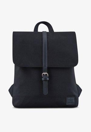 Mochila de tela negra con cierre de solapa, correa de hebilla en el frente, asa superior y parche de marca en la esquina inferior derecha.