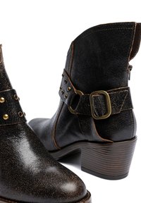 Botines de cuero negro con acabado texturizado, con hebilla y tachuelas en tono dorado, punta puntiaguda y tacón apilado de madera.