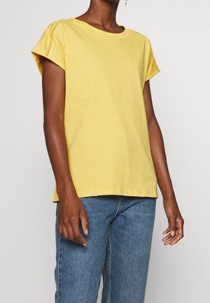 Geel katoenen T-shirt met korte mouwen, met uitsnijdingen op de schouders, gecombineerd met blauwe denim jeans.