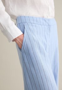 Pantalones a rayas azul claro hechos de tela ligera, con un corte relajado y bolsillos laterales, combinados con una camisa blanca de botones.