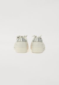 Weiße Sneakers mit silbernen metallischen Akzenten an der Ferse. Runde Zehenform, schnürsenkelloses Design, strukturierte Gummisohle, minimalistischer Stil.