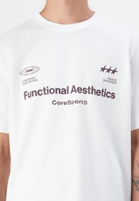 White cotton t-shirt featuring a crew neck, short sleeves, and dark text. Design includes logos and phrases related to sports.